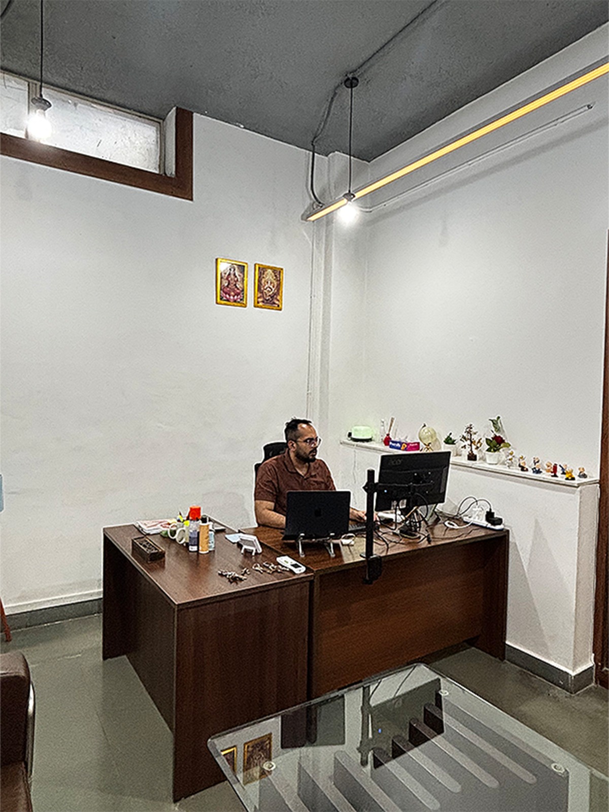 The founder at his desk — laptop, monitor, the operating bay just outside the door.